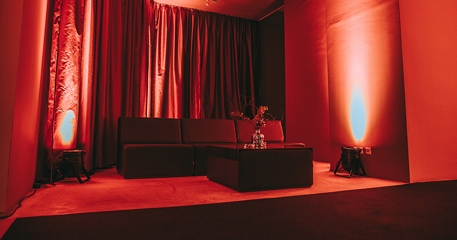 couchelemente_palais-berg - Palais Wertheim Wien Red-lit lounge area with a black sectional sofa, matching ottoman, and a glass vase on the coffee table.