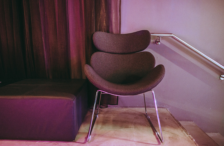 designersessel_palais-berg - Palais Wertheim Wien Modern curved lounge chair with chrome legs in a purple-lit corner beside a purple bench.