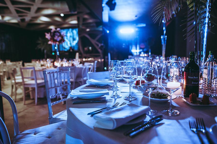 galatische_palais-berg - Palais Wertheim Wien Elegant banquet table set for a formal dinner with white tablecloths, wine glasses, and bottles under blue lighting on stage