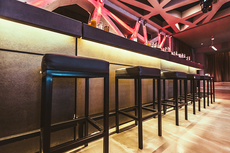 hocker - Palais Wertheim Wien Long bar with black stools lined up along a glowing countertop in a modern lounge or club setting, bottles visible on the back rail.