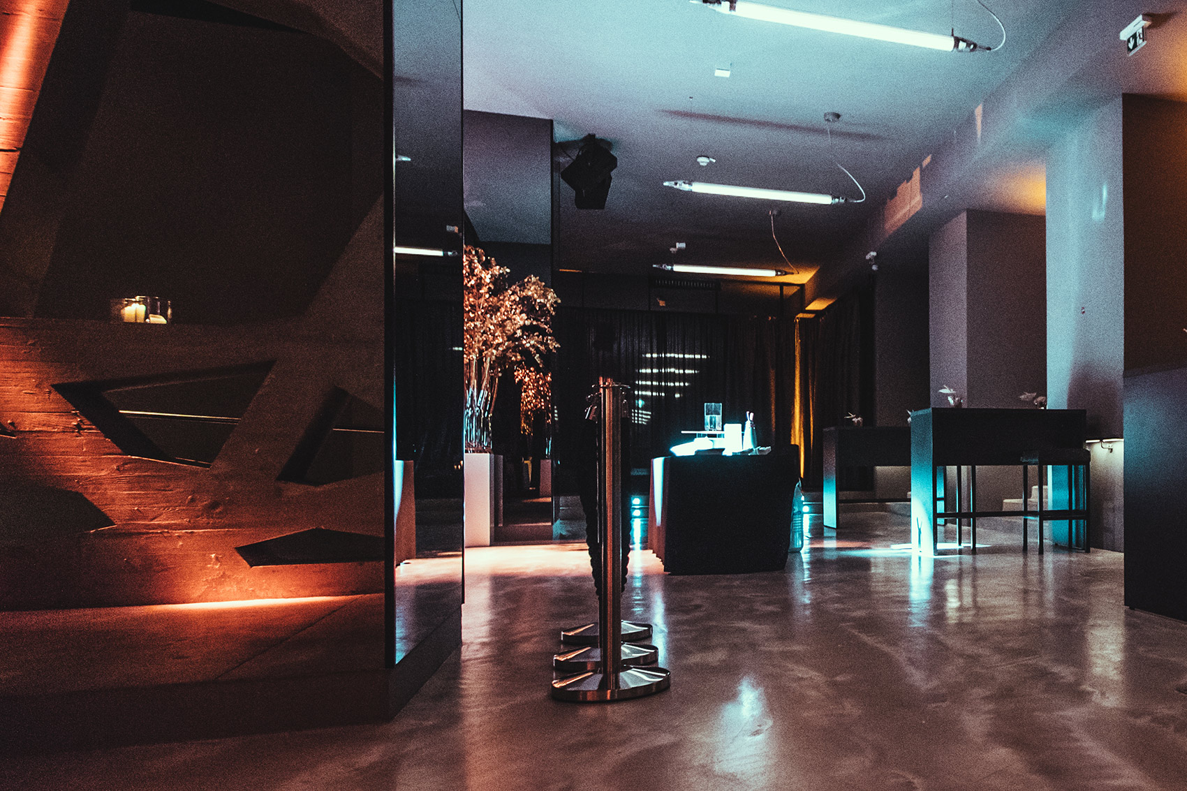 kordeln_schildsteher-palais-wertheim - Palais Wertheim Wien Dim, modern lounge or club interior with blue and orange lighting, a polished concrete floor, and high tables in the background.