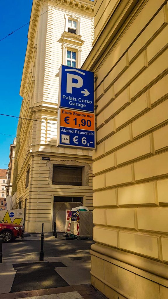 Blue parking sign on a beige corner building reads 'Palais Corso Garage' with rate panels: first hour €1,90 and evening flat rate €6,- on a sunny street.