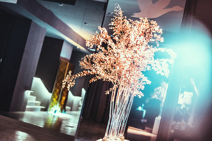 vasen-mit-blumen_palais-berg - Palais Wertheim Wien Decorative dried flower arrangement in tall glass vases on a modern, dimly lit interior with colorful lighting.